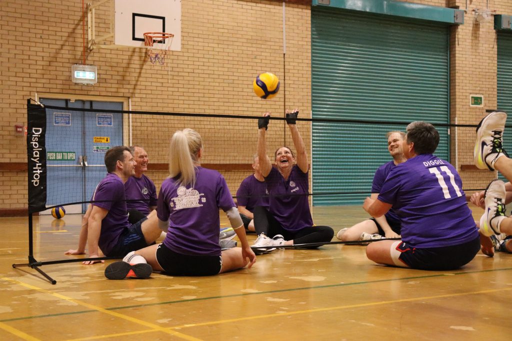 Participants reach for a yellow ball as they play sitting Volleyball together at the Portland Centre. 