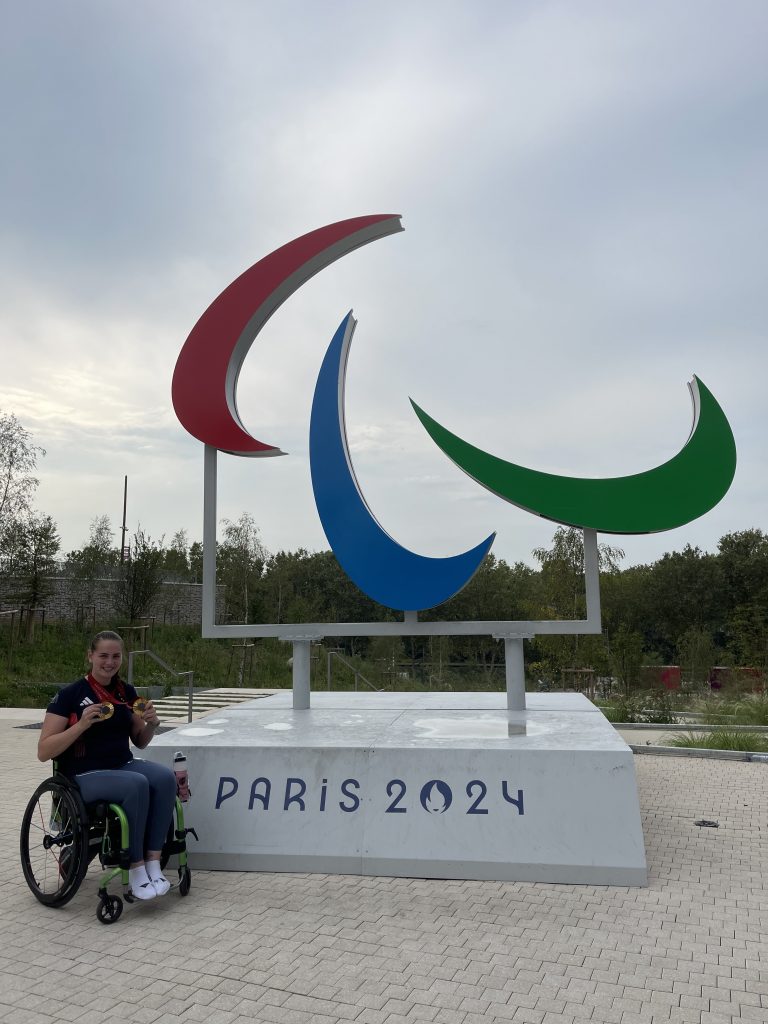 Tully Kearney poses in a wheelchair next to an erected statue of the Paris Paralympics logo.